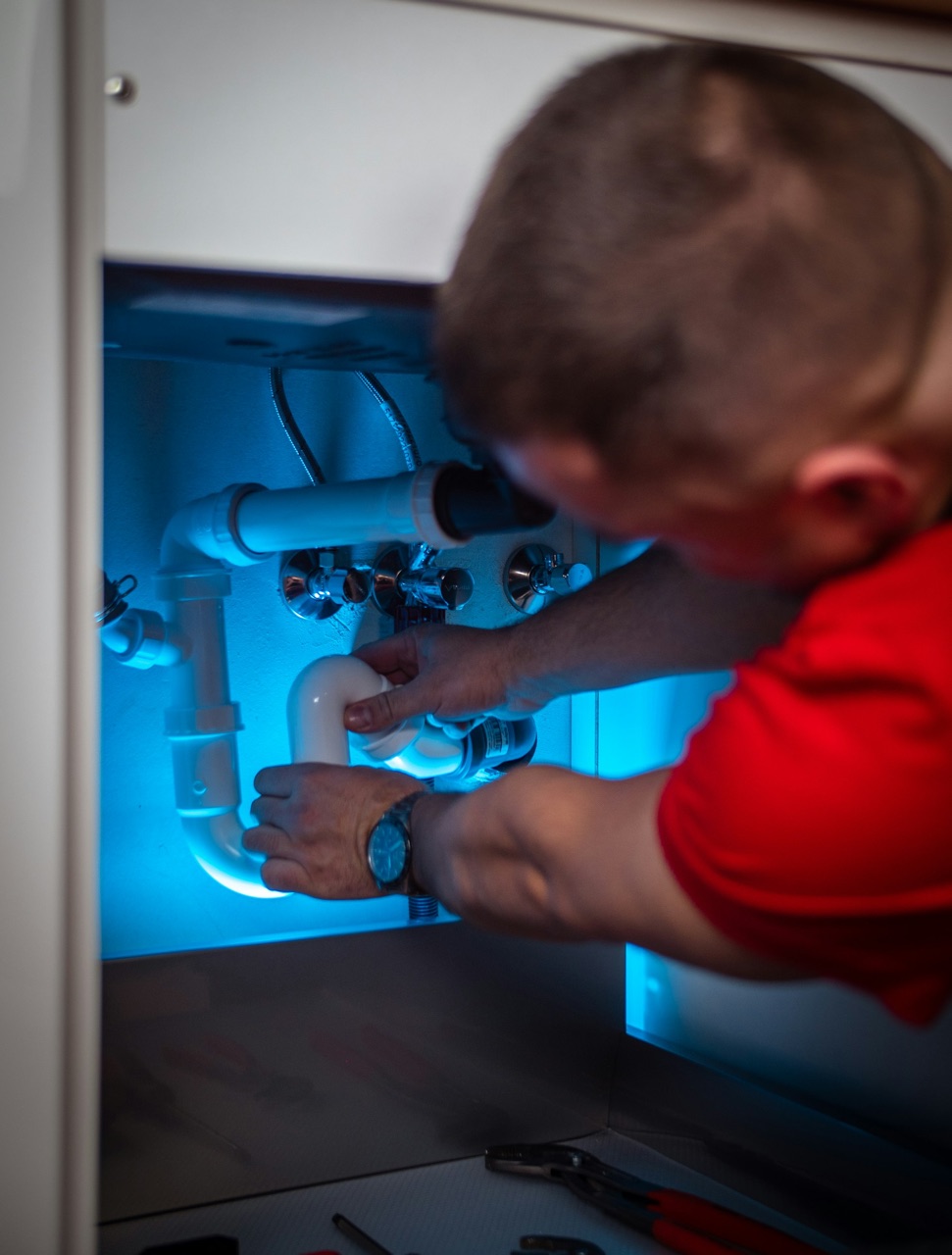 Plumber repairing a pipe under a sink after an after-hours call